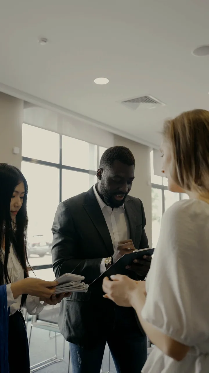 Event hosts sign guests in at a conference: one checks names on a clipboard while another hands out lanyards.