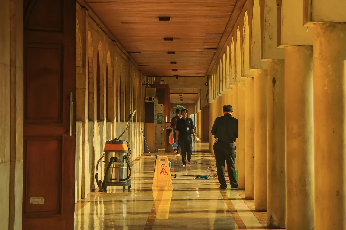 A cleaning crew at work in a long, sunlit colonnade.
