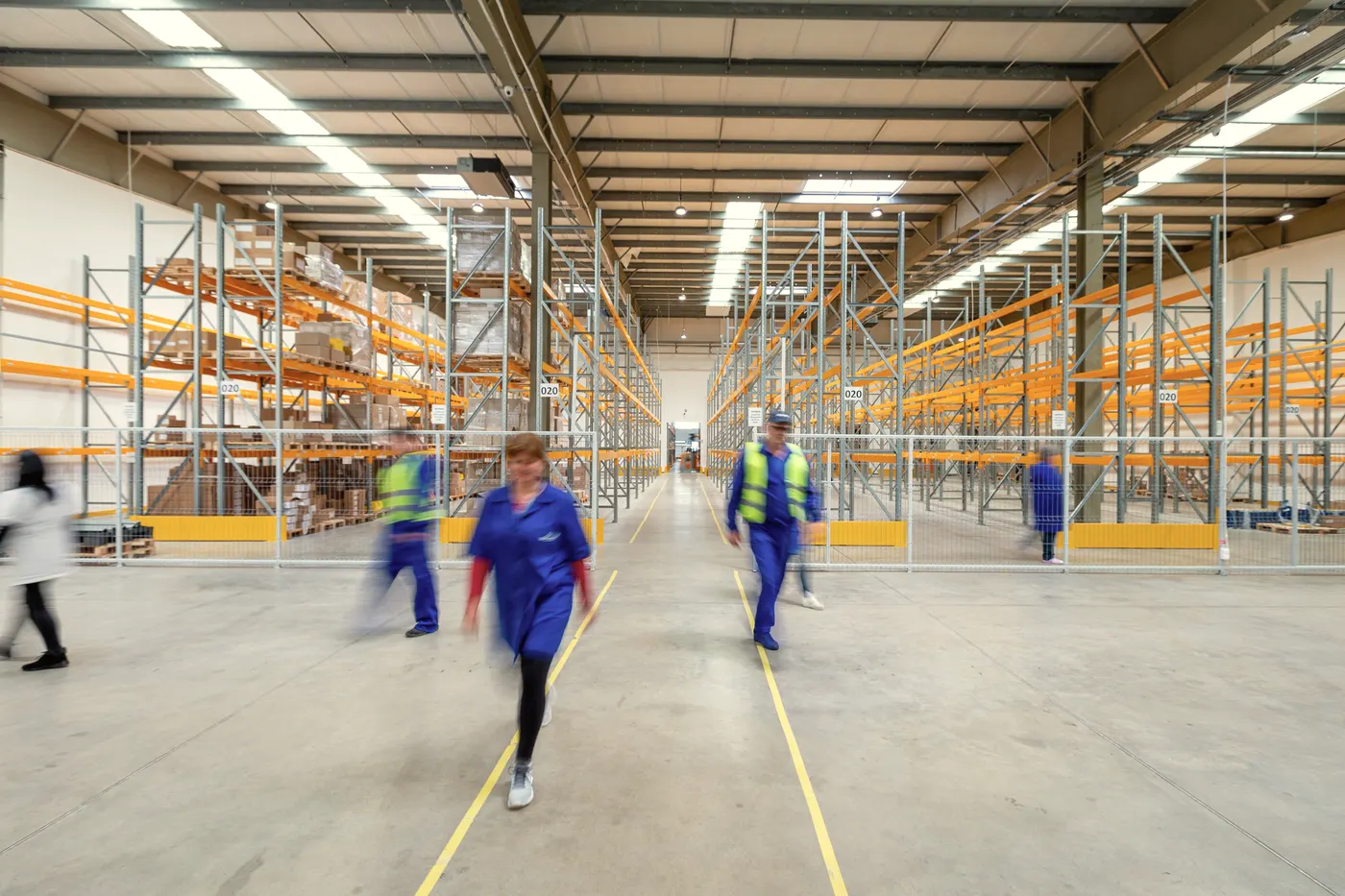 Staff walk the aisle of a large warehouse.