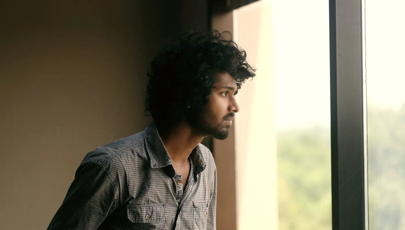 A young man looks out of a window, thinking ahead.