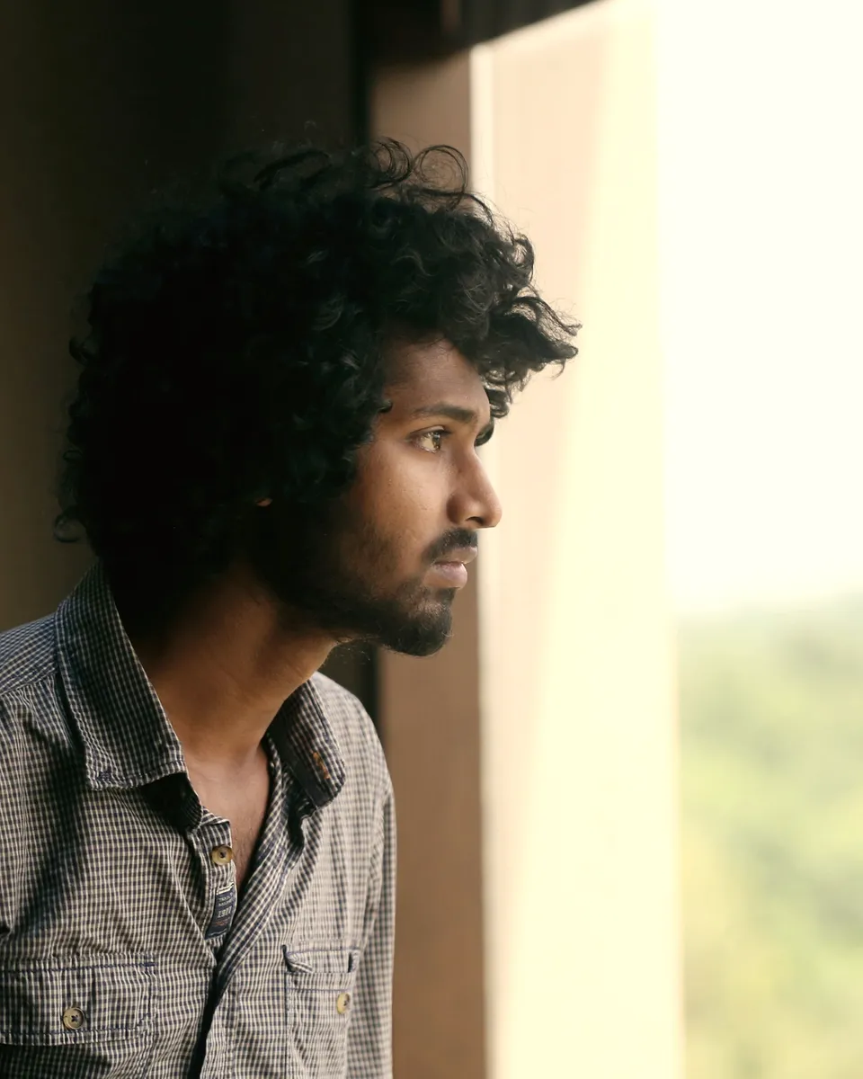 A young man looks out of a window, thinking ahead.